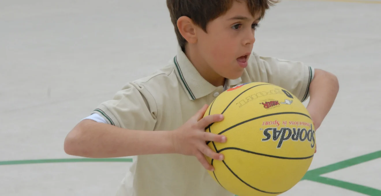 Enfant en tenue de basket avec un ballon sur un terrain en intérieur