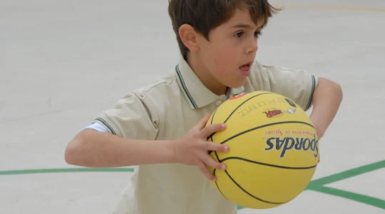 Enfant en tenue de basket avec un ballon sur un terrain en intérieur